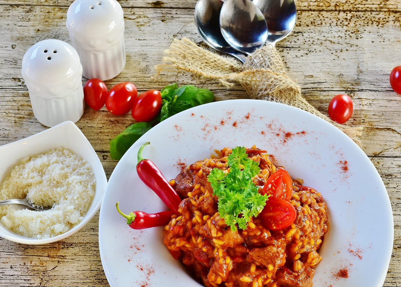 Un piatto fondo di porcellana bianca contiene orzotto cremoso di colore avorio, con verdure di stagione, gocce di olio d'oliva e una grattugia di formaggio grattugiato in superficie, vassoio di legno