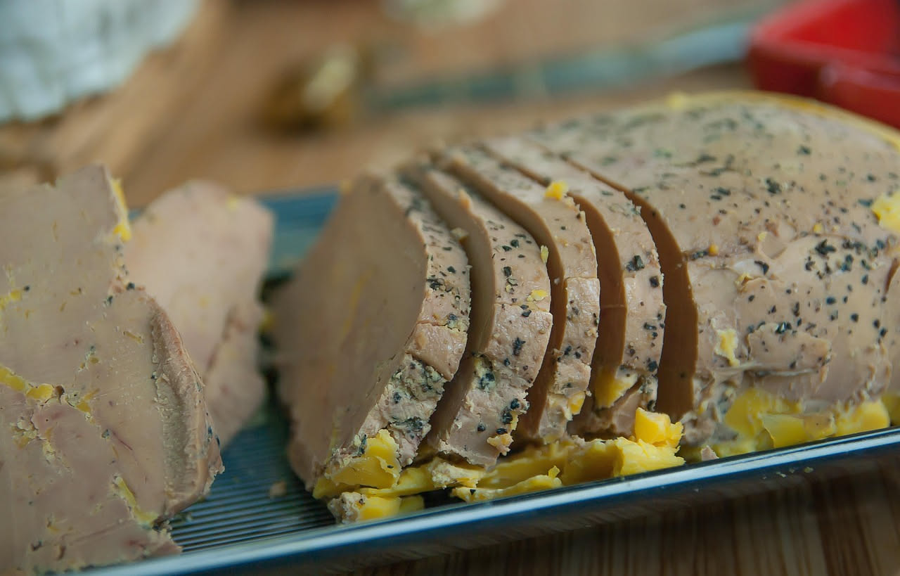 Pâté di fegato cremoso di colore marrone chiaro, sparso su pane tostato, decorato con una foglia di timo fresco su piatto bianco