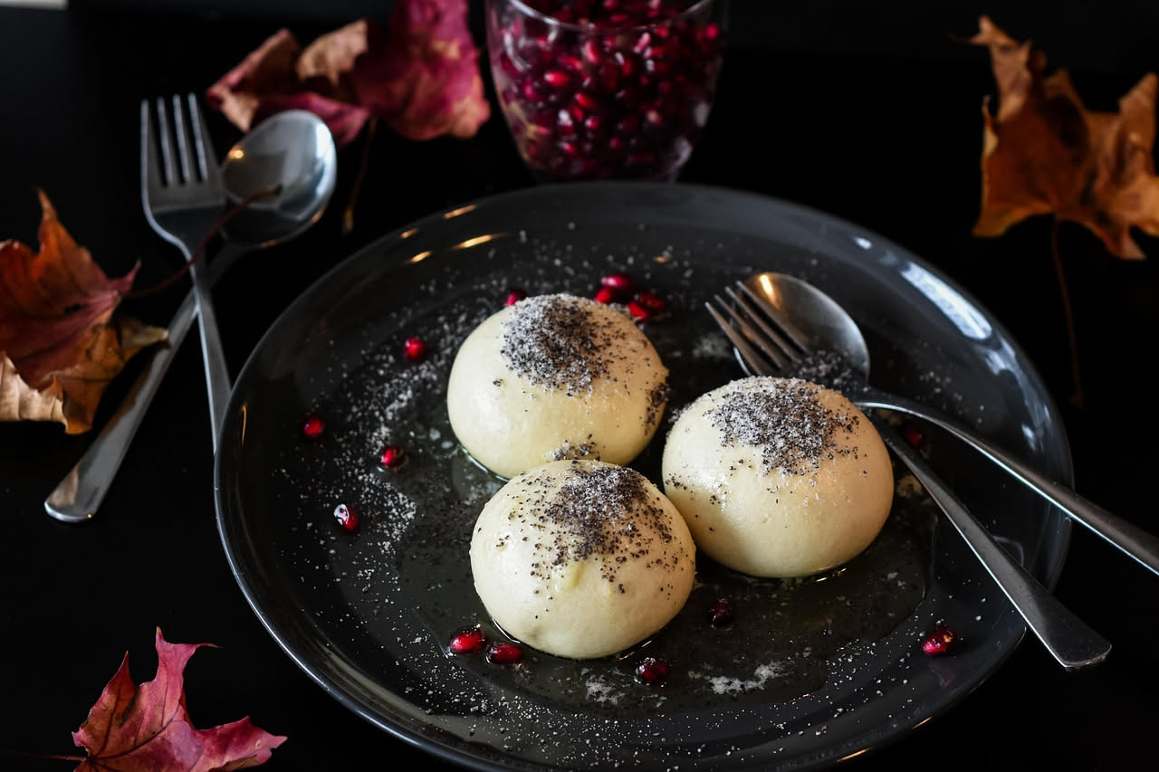 Palle di ricotta bianche e rotonde ricoperte di zucchero su un piatto bianco, con una tazza di caffè sfuocato sullo sfondo