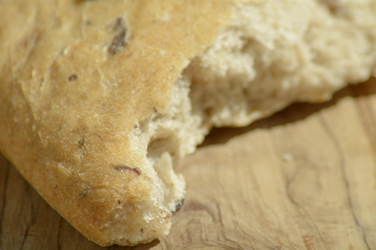 Pan di ramerino dorato su piatto di ceramica bianca, foglie di rosmarino fresco sparse intorno, texture irregolare e rustica del biscotto