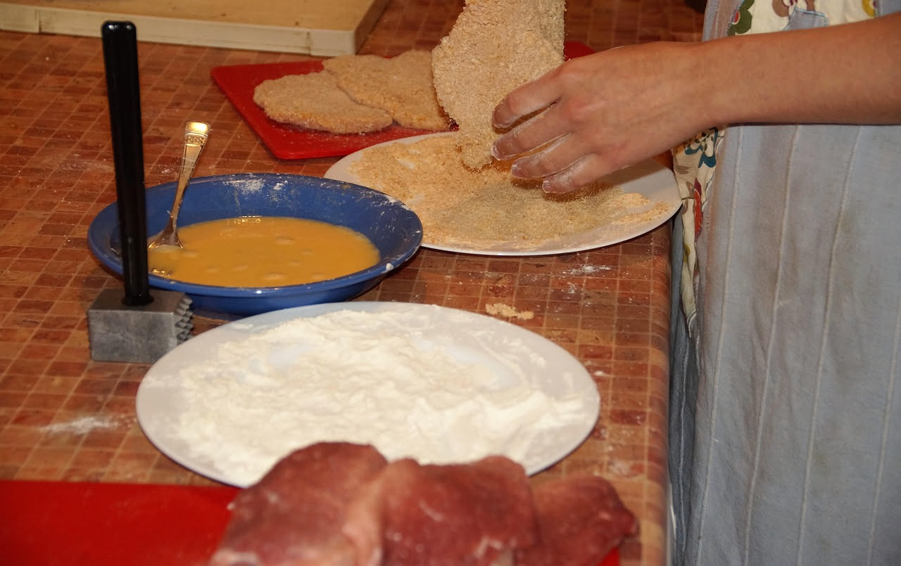 Panata in ciotola di ceramica bianca, colore marrone dorato, consistenza cremosa e densa, guarnita con parmigiano grattugiato e fettina di pane croccante, cucchiaio di legno dentro