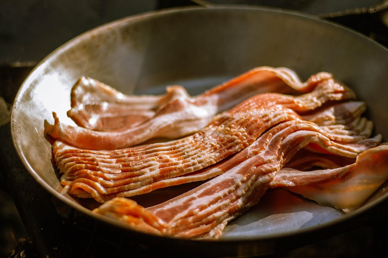 Fette di pancetta affumicata dal colore marroncino uniforme, leggermente lucide, impilate nel piatto bianco, contorno di prezzemolo fresco verde