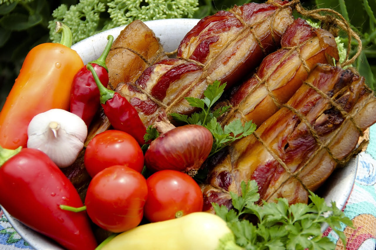 Pancetta aretina affumicata a fette, colore dorato e marrone, disposta su un tagliere di legno con la pelle ancora visibile