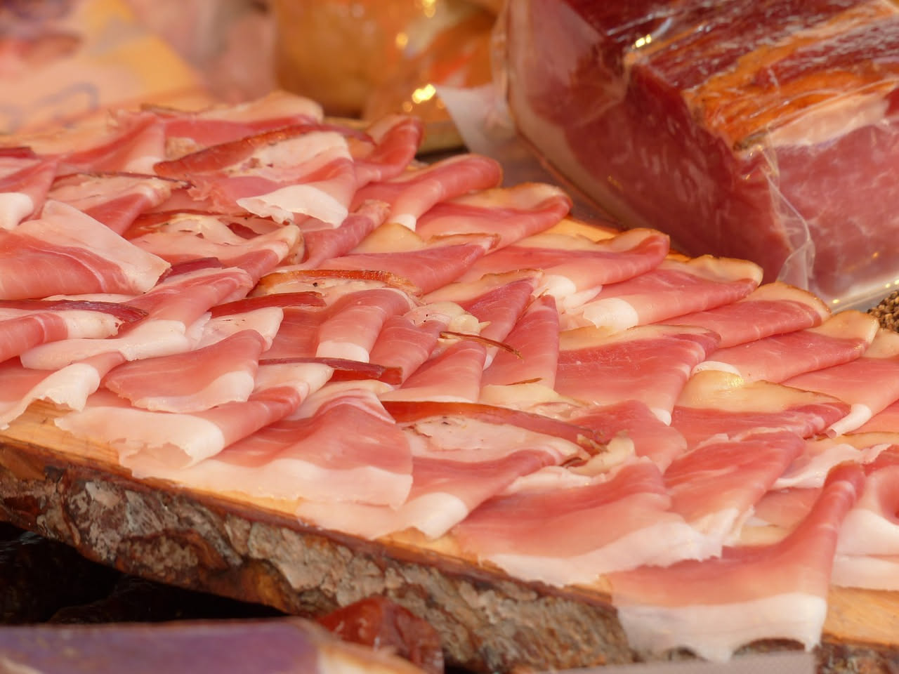 Pancetta di Piacenza affettata su un tagliere di legno con coltello e spezie, vista dall'alto con luce naturale