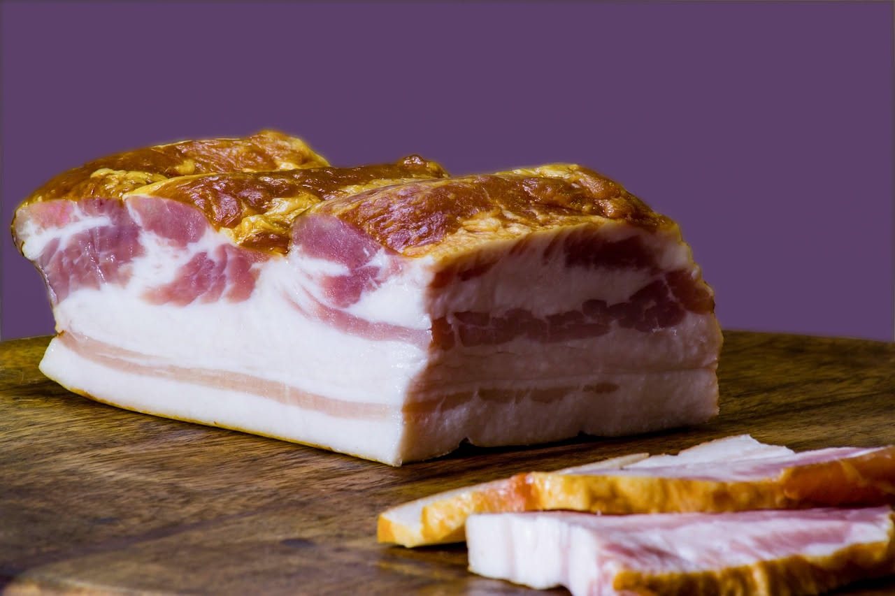 Fette di pancetta di Pienza affumicata e stagionata, tagliate sottili, con striature di grasso bianco su sfondo di legno naturale