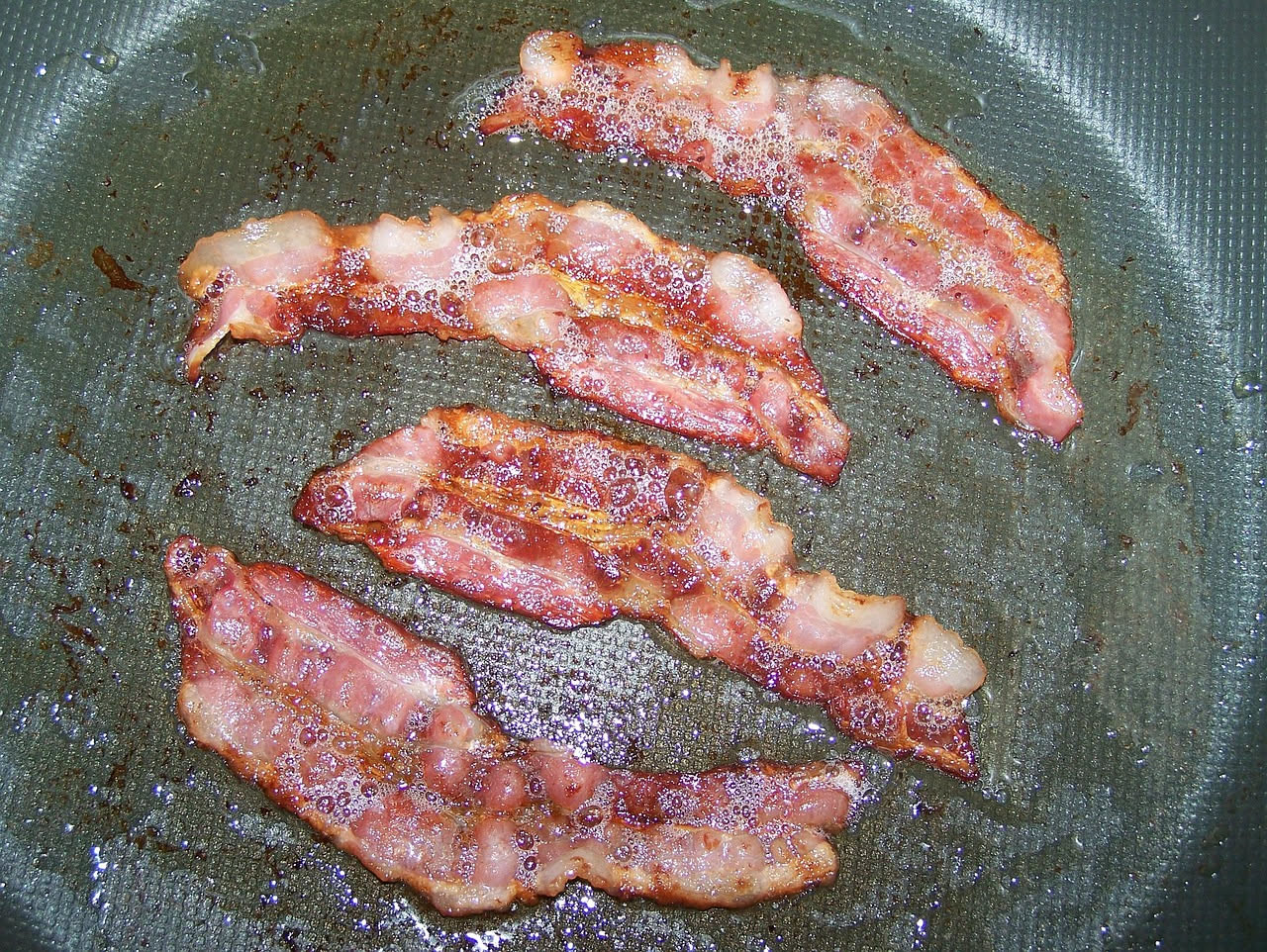 Fette sottili di pancetta veneta dal colore rosato con venature di grasso bianche, affumicate e lucide, disposte su un piatto bianco