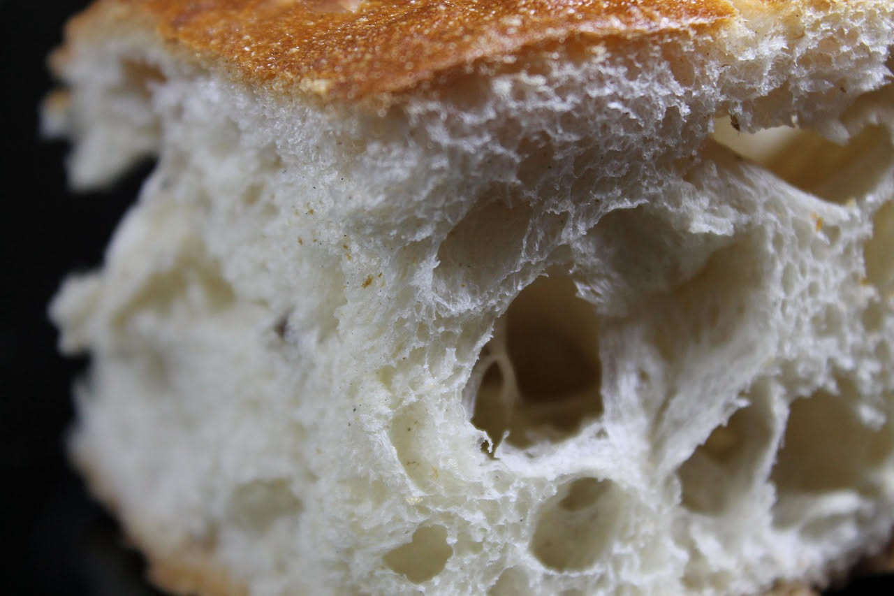 Pane intero appena sfornato con crosta dorata e screpolata, tagliato a metà per mostrare la mollica bianca e soffice, vapore ancora visibile, posato su una tavola di legno scuro