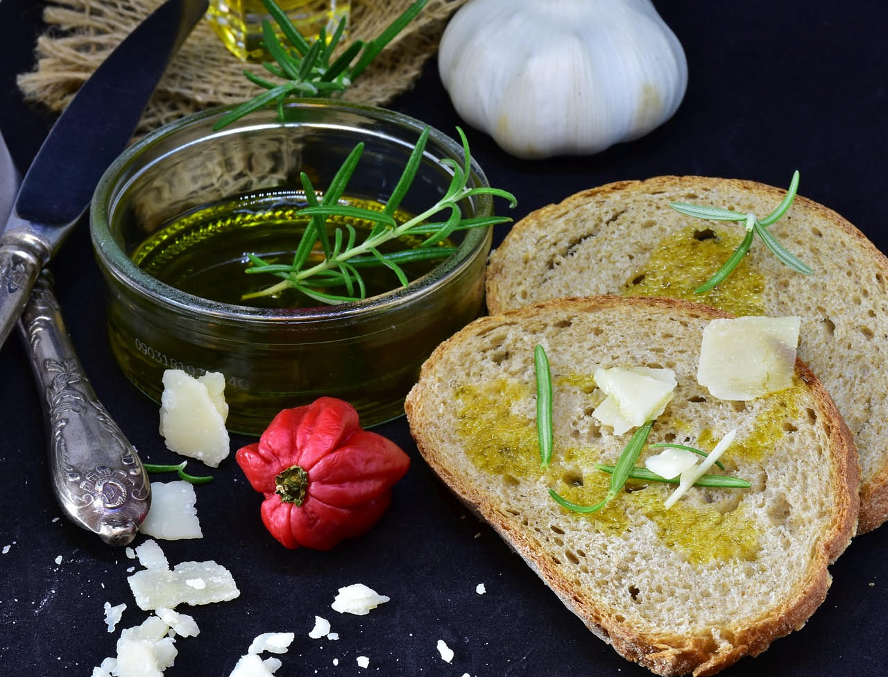 Fette di pane tostato dorate con aglio tritato e gocce di olio extravergine, su piatto bianco, con prezzemolo fresco ai lati
