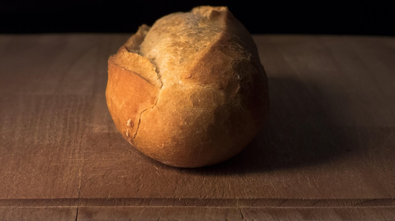 Pane unto dorato con superficie lucida e leggermente oleosa, tagliato a metà mostrando la mollica soffice, servito su una tavola in legno con una ciotola di olio extravergine accanto