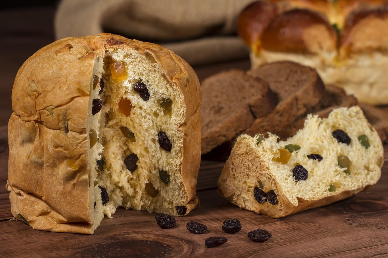 Panettone bergamasco intero appena sfornato, con forma tonda e bombata, superficie dorata e lucida, canditi colorati visibili nella miga, affettato per mostrare la consistenza soffice e gli ingredient