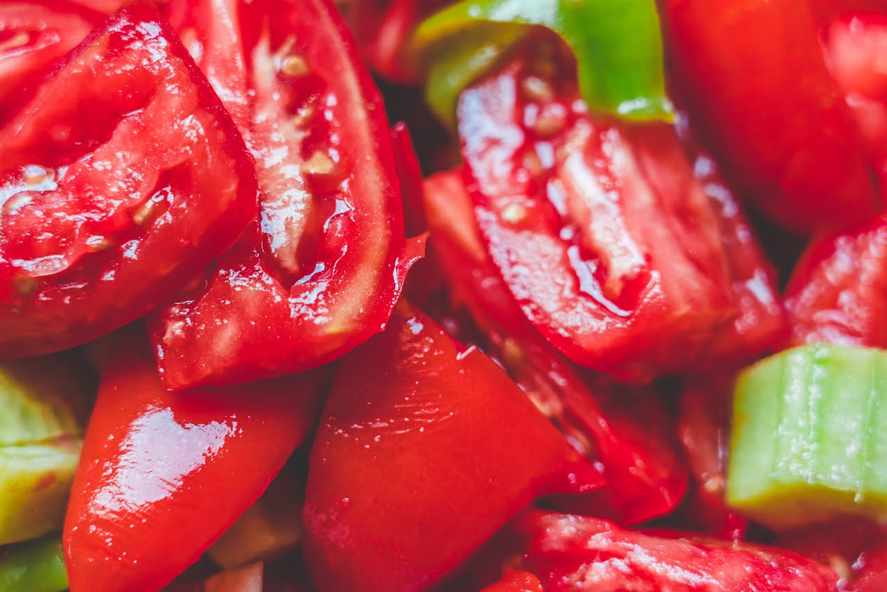 Pani ca tomatigus appena sfornati, pani panini rotondi dorati con spaccatura superiore, pieni di pomodori rossi e cipolla violastra visibili, serviti su piatto bianco con foglie di origano fresco