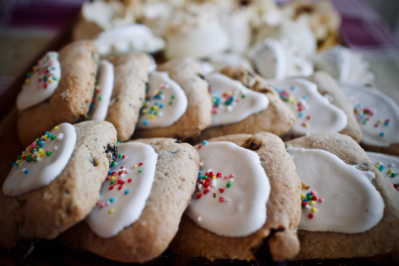 Papassini allineati su carta da forno, biscotti color nocciola chiaro, dalla forma leggermente obliqua, con superficie punteggiata di semi di anice, sfondo neutro bianco