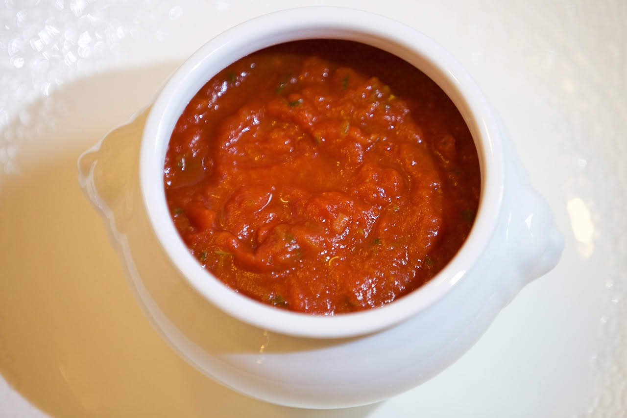 Ciotola di pappa al pomodoro rosso cremosa con foglia di basilico fresco, pane raffermo spezzettato accanto, olio extravergine d'oliva versato sopra