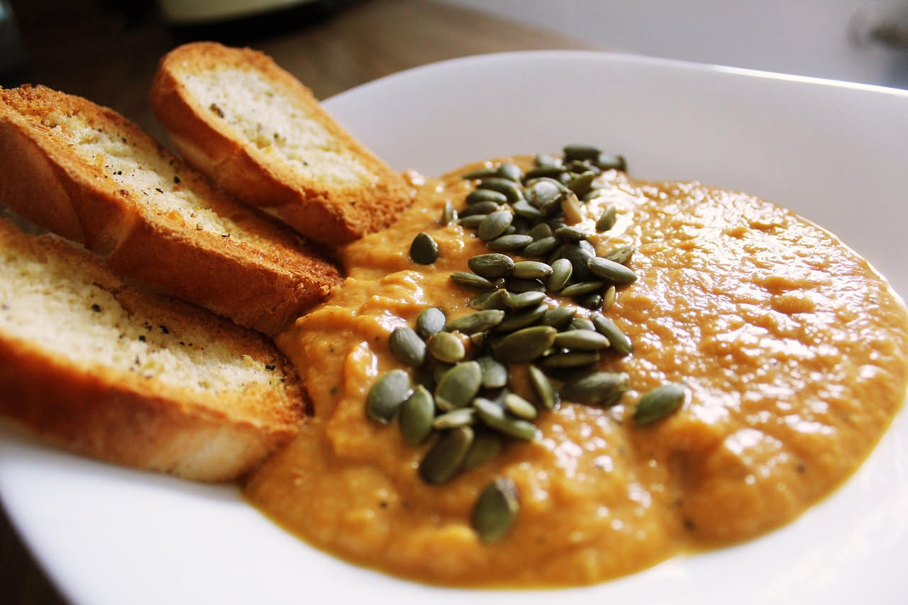 Una ciotola bianca di pappa di pane e fagioli di colore beige-marrone chiaro, cremosa e densa, con le bucce dei fagioli visibili in superficie, guarnita da un filo di olio verde e pepe nero, piatto le