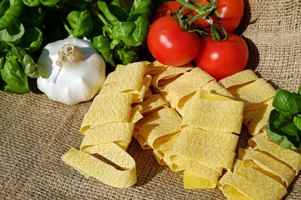 Ciotola bianca di ceramica con pappardelle cotte in brodo trasparente, pasta larga visibile sulla superficie, un filo di olio d'oliva verde, prezzemolo fresco tritato sparse, bordo della ciotola con a