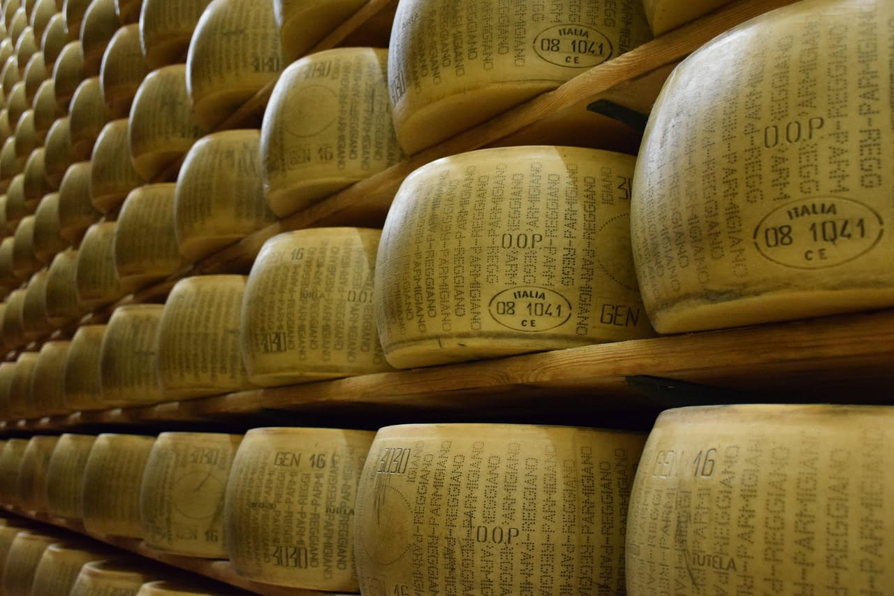 Fetta di Parmigiano Reggiano giovane color paglierino con pasta liscia e cremosa su un tagliere di legno accanto a un coltello per formaggi