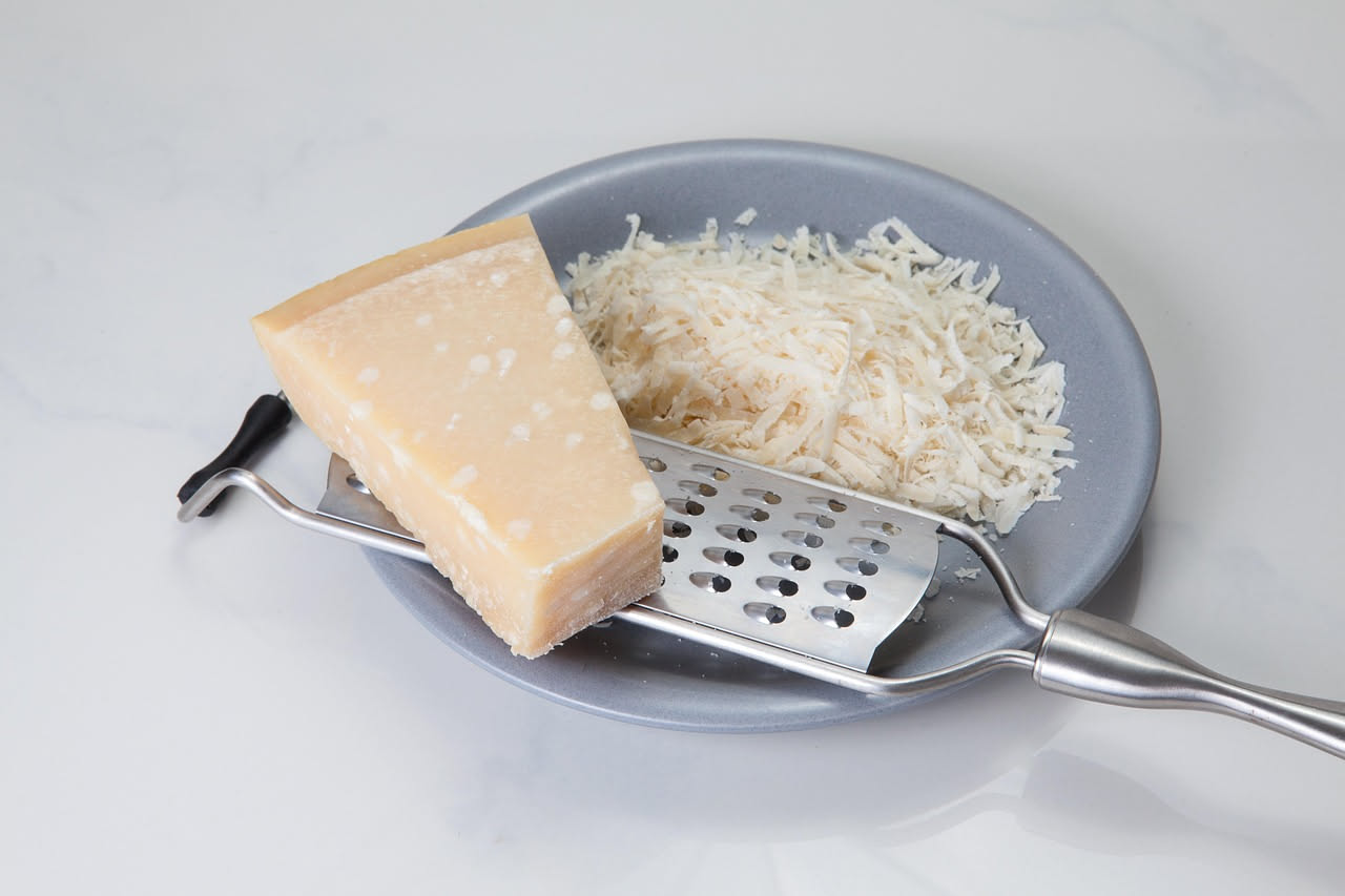 Fetta di Parmigiano Reggiano stagionato spezzata a mano su un piatto bianco, con cristalli bianchi visibili sulla superficie e colore giallo paglierino intenso