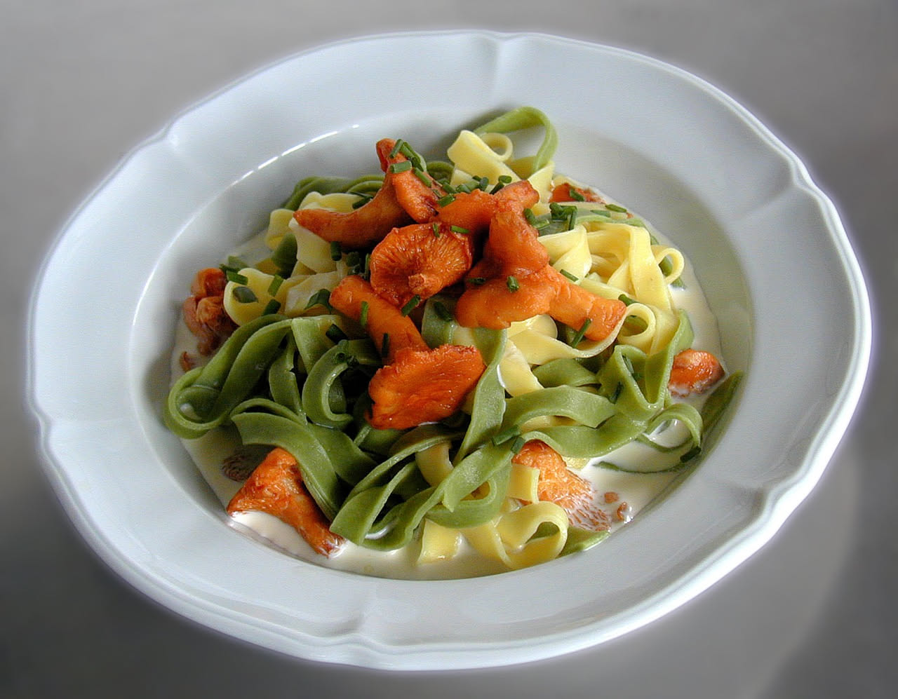 Piatto di pasta alle penne condita con funghi porcini trifolati color marrone dorato, salsa cremosa bianca, prezzemolo verde fresco spolverato, servita in piatto bianco fondo.