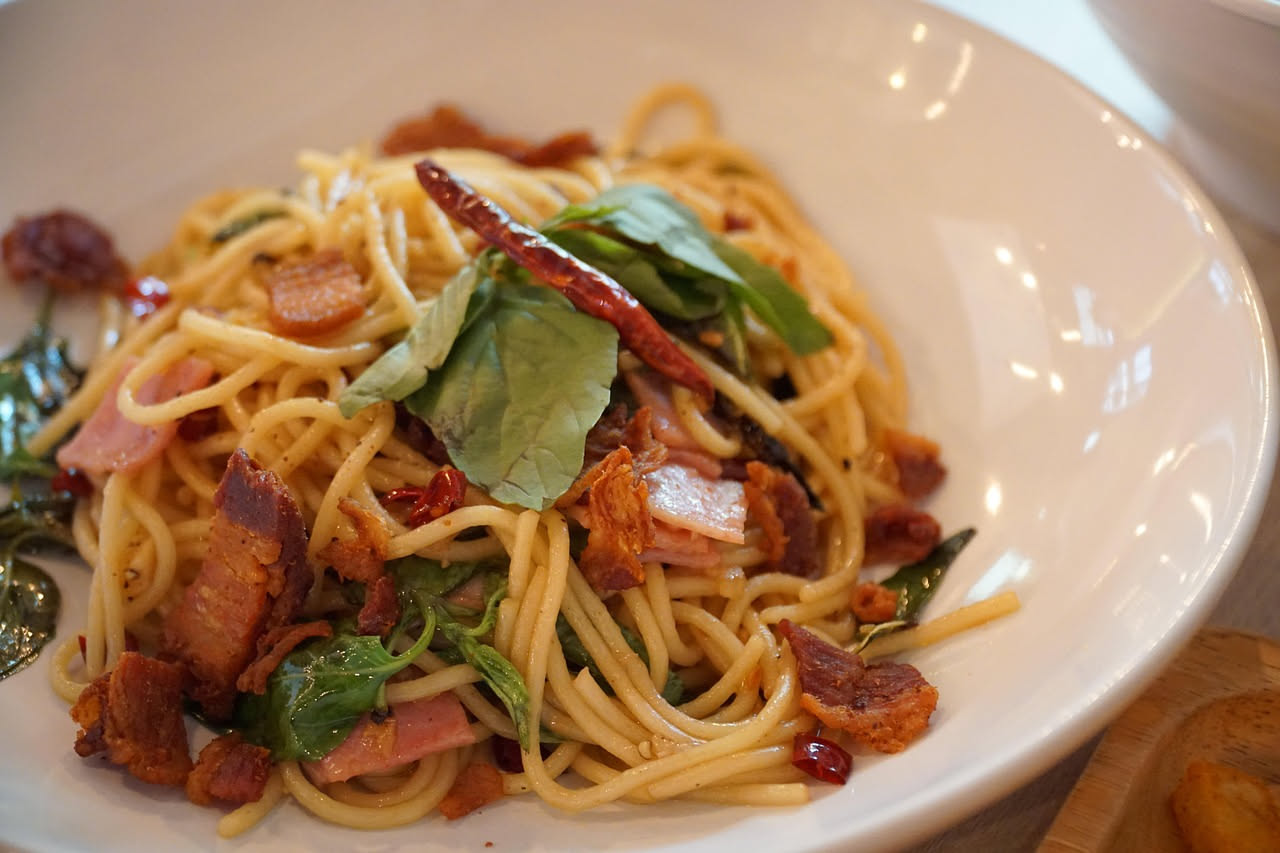 Piatto di spaghetti alla carbonara con cremosità bianca, pepe nero visibile, guanciale dorato a listarelle, pecorino grattuggiato, servito in piatto bianco fondo.