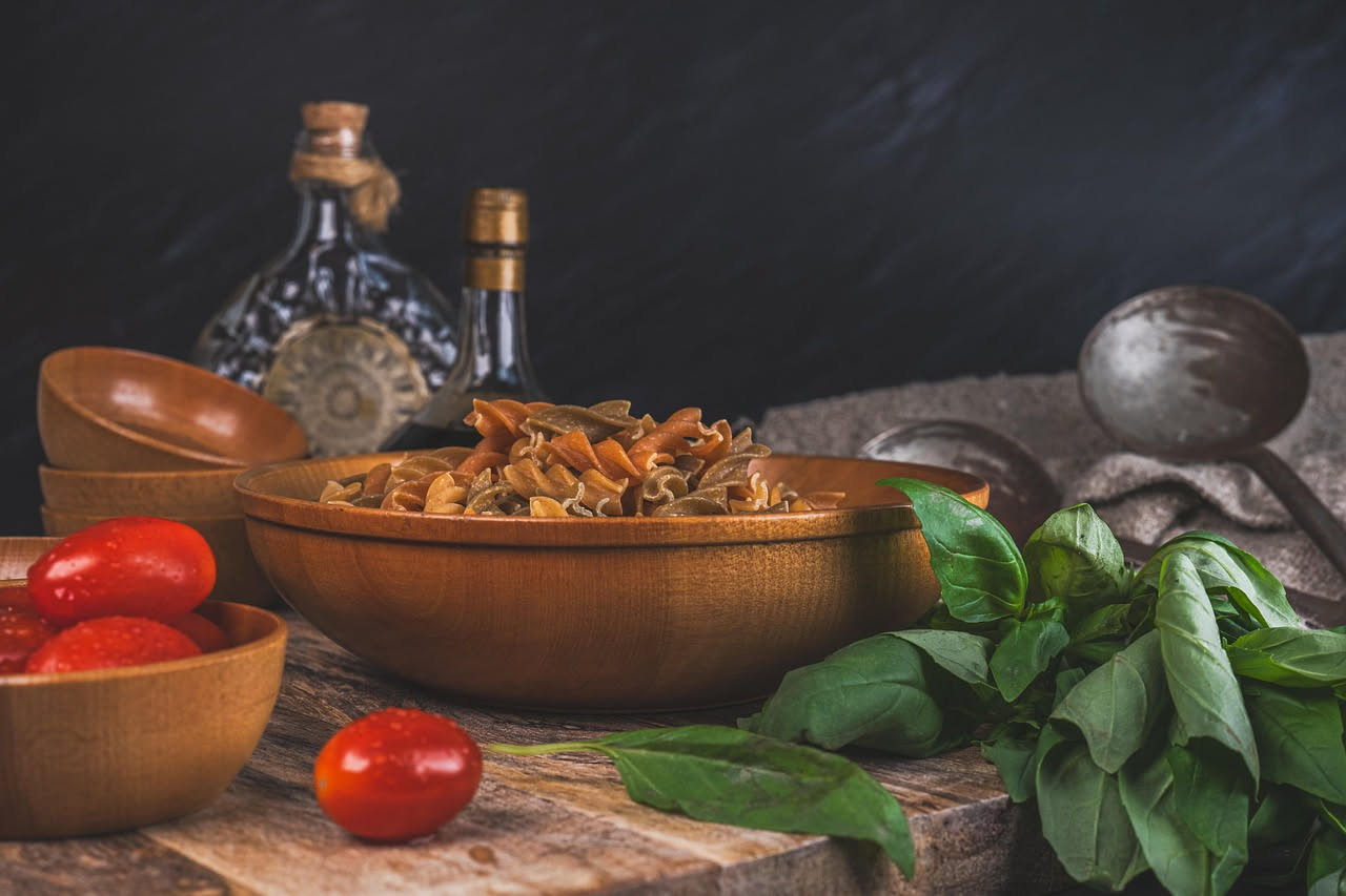 Piatto di pasta alle melanzane con melanzane dorate fritte, ricotta salata grattugiata bianca, sugo rosso di pomodoro, foglie di basilico verde fresche, ritratto dall'alto in luce naturale