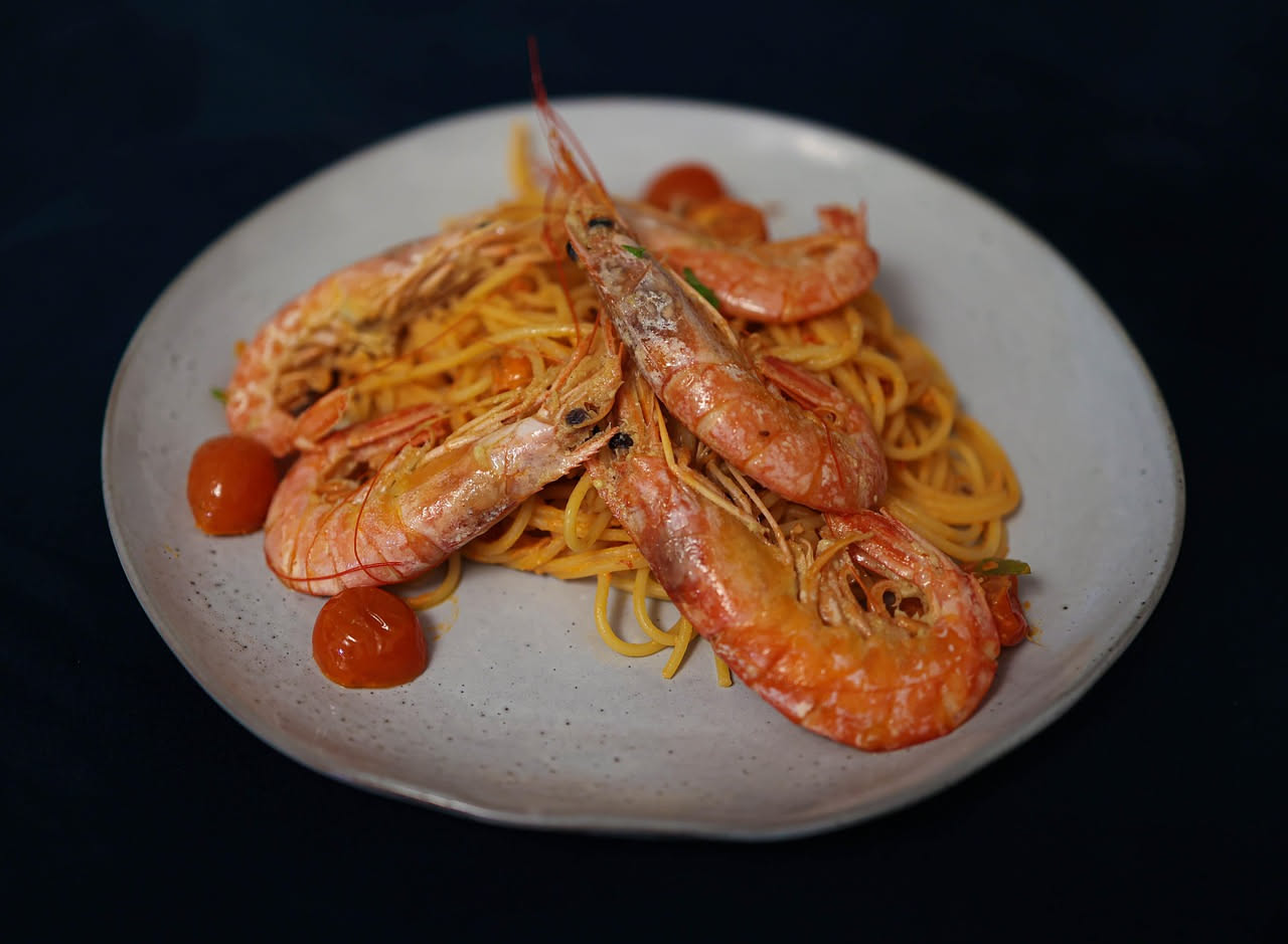 Piatto di pasta linguine con scampi rossi e interi, olio brillante, prezzemolo verde fresco, limone, su tavola di legno scuro