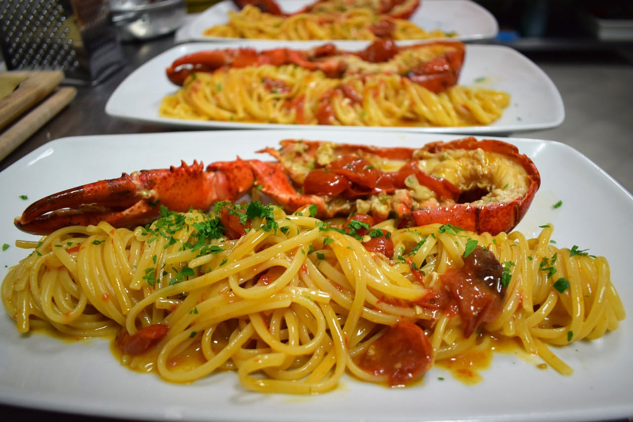 Piatto di pasta con ricci di mare: spaghetti gialli raccolti in nido, conditi con ricci di mare di colore arancio intenso, aglio dorato e prezzemolo fresco verde, serviti in piatto bianco su tavolo di