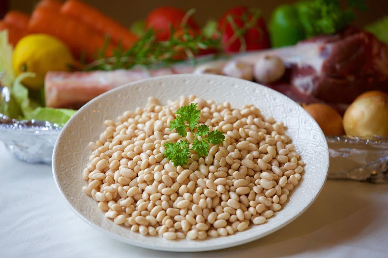 Ciotola di ceramica bianca con pasta e fagioli modicani: fagioli cannellini interi in brodo rosato, pasta ditalini, pomodoro sbriciolato in superficie, filo d'olio verde oliva, prezzemolo fresco trita