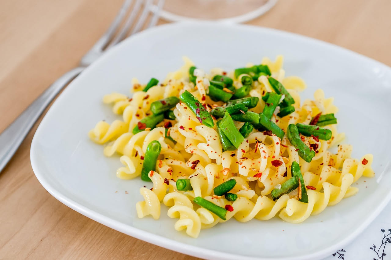Ciotola bianca con pasta e fagioli fredda, olio d'oliva dorato, prezzemolo fresco e pomodori rossi su fondo di legno chiaro