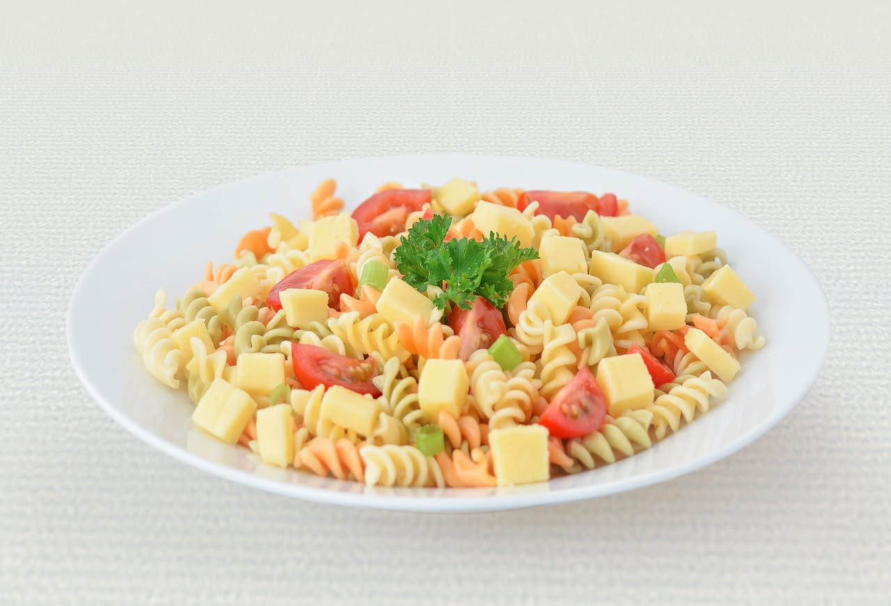 Una ciotola di pasta penne bianche con cubetti di pomodoro rosso brillante, foglie di basilico verde e filo di olio d'oliva dorato in superficie, servita su un piatto bianco