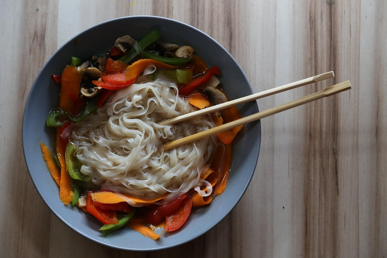 Zuppa di pasta in brodo trasparente con carote, zucchine, sedano e pomodori, pasta corta visibile nel liquido, servita in ciotola bianca su tavolo di legno