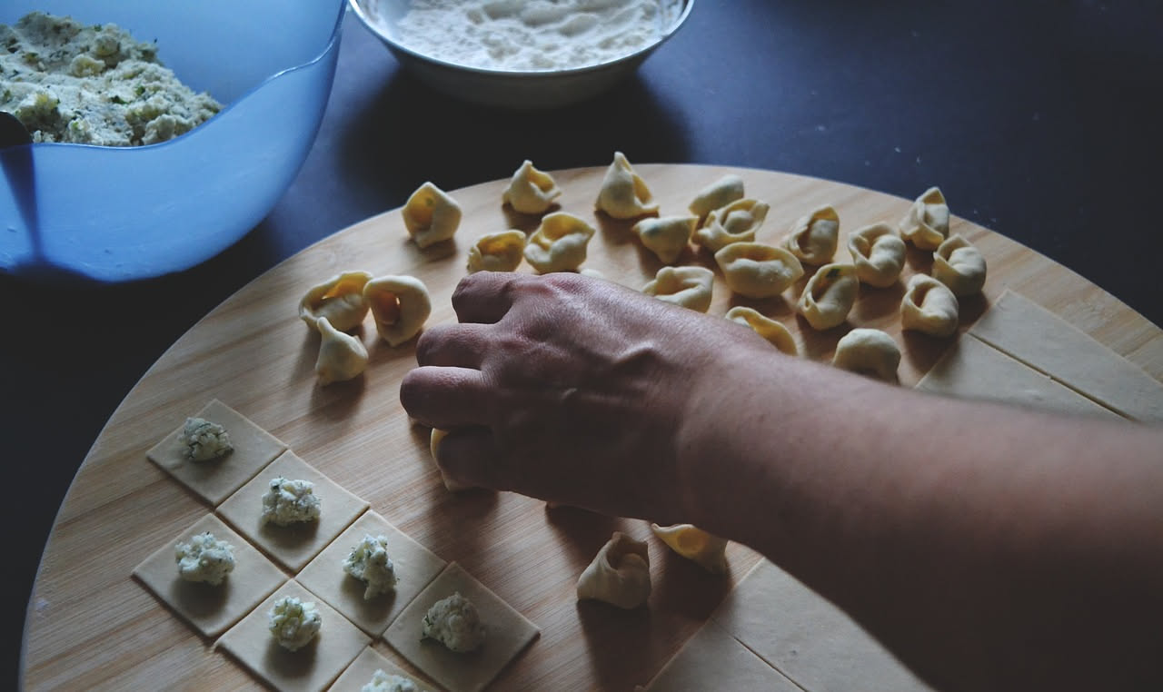 Piatto di pasta ripiena con ricotta e spinaci, quattro ravioli tondi su fondo bianco impiattati con burro fuso e parmigiano grattugiato, vapore leggero visibile