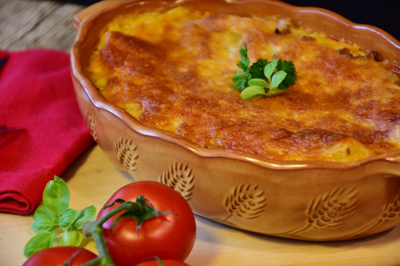 Un piatto di ceramica bianca con pasticcio di lepre: carne scura e tenera, verdure morbide, salsa marrone ricca, decorato con un ciuffo di prezzemolo fresco. Contorno di pane tostato. Luce naturale di