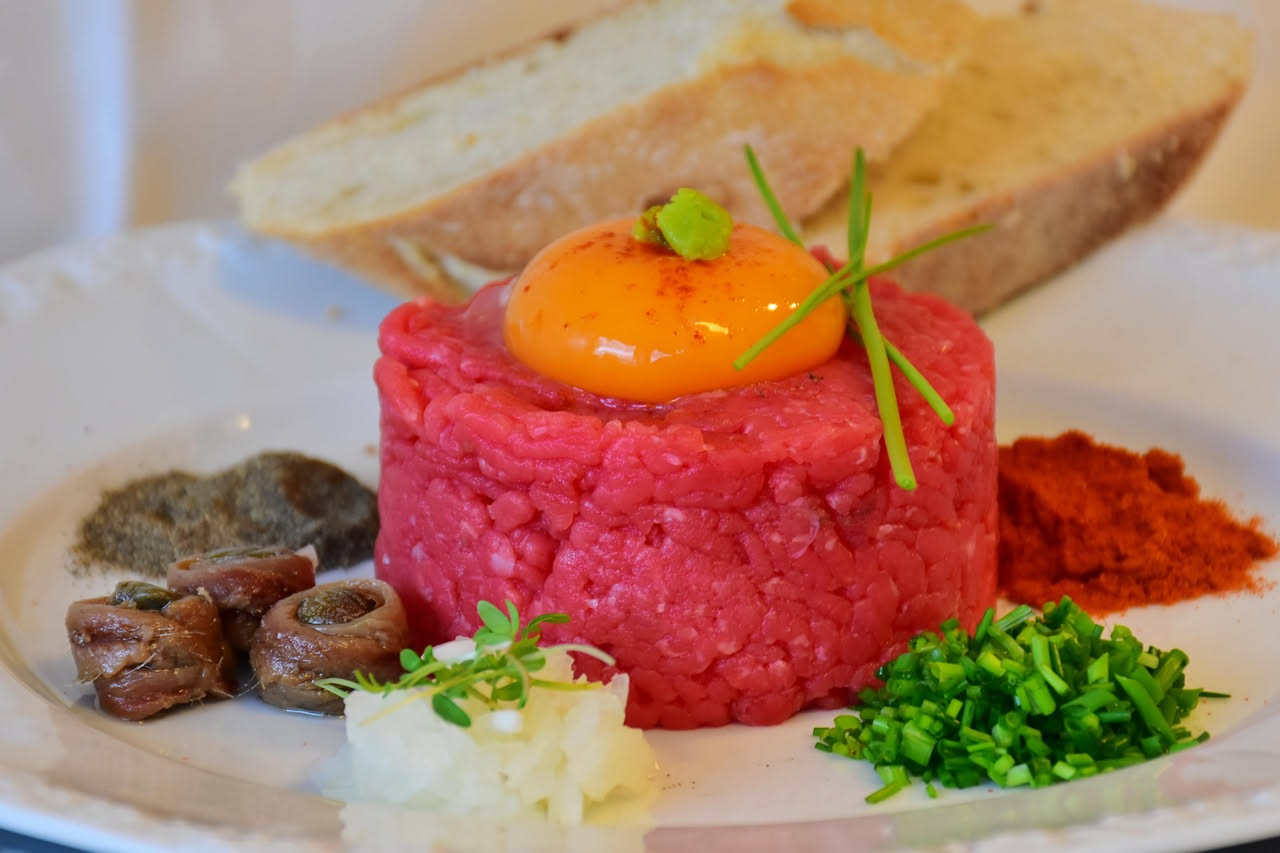 Paté di selvaggina color marrone cioccolato in una ciotola bianca, con un coltello da burro appoggiato, accompagnato da fette di pane tostato e una foglia di rosmarino fresco