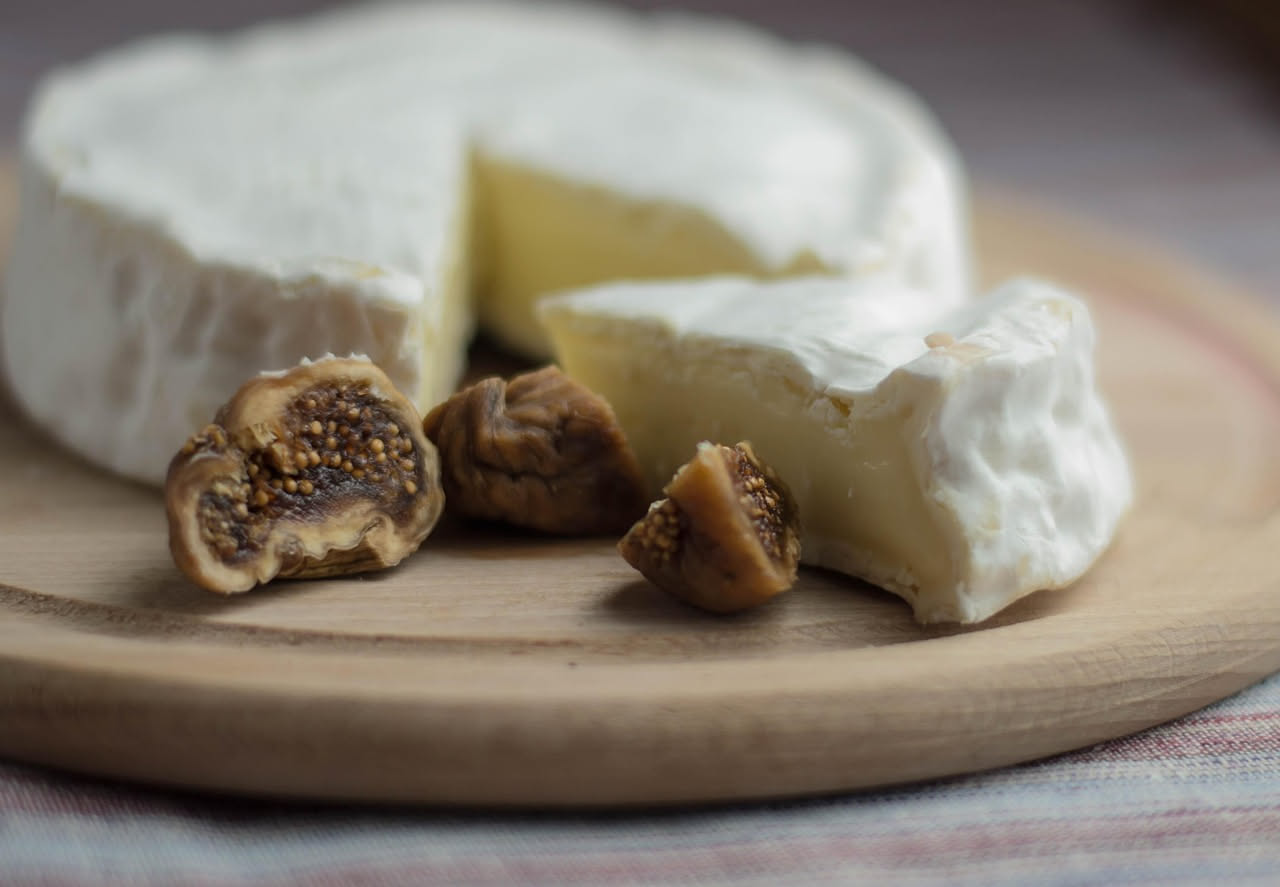 Fettine di pecorino fresco bianco cremoso affiancate a quarti di fichi viola freschi su un piatto bianco, con miele che cola su un lato