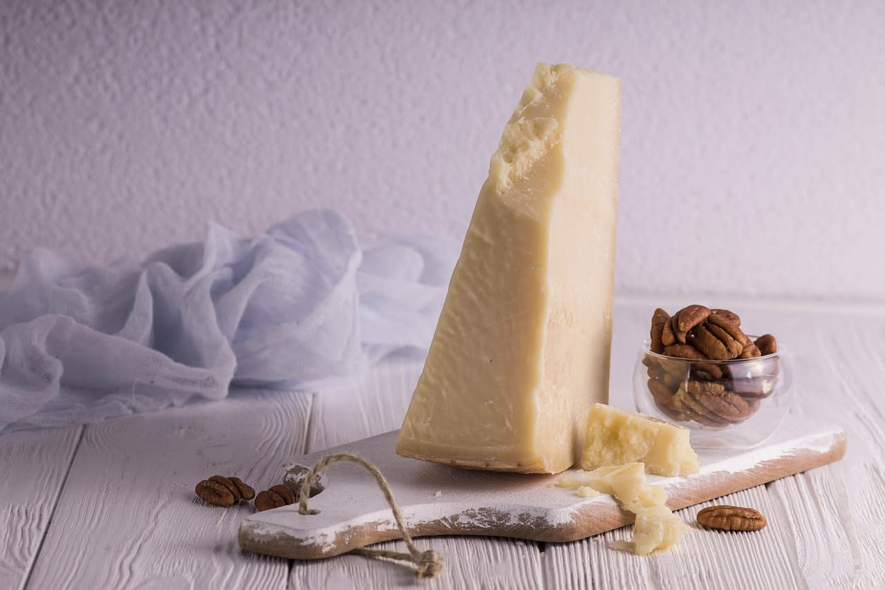 Pecorino romano stagionato giallo dorato, spezzettato su un tagliere di legno scuro con coltello seghettato, accanto a qualche grano di pepe nero