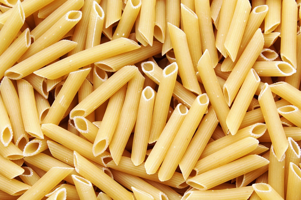 Pennette rosse di pomodoro servite in piatto bianco, condite con olio, peperoncino rosso tritato visibile in superficie, guarnizione di prezzemolo fresco