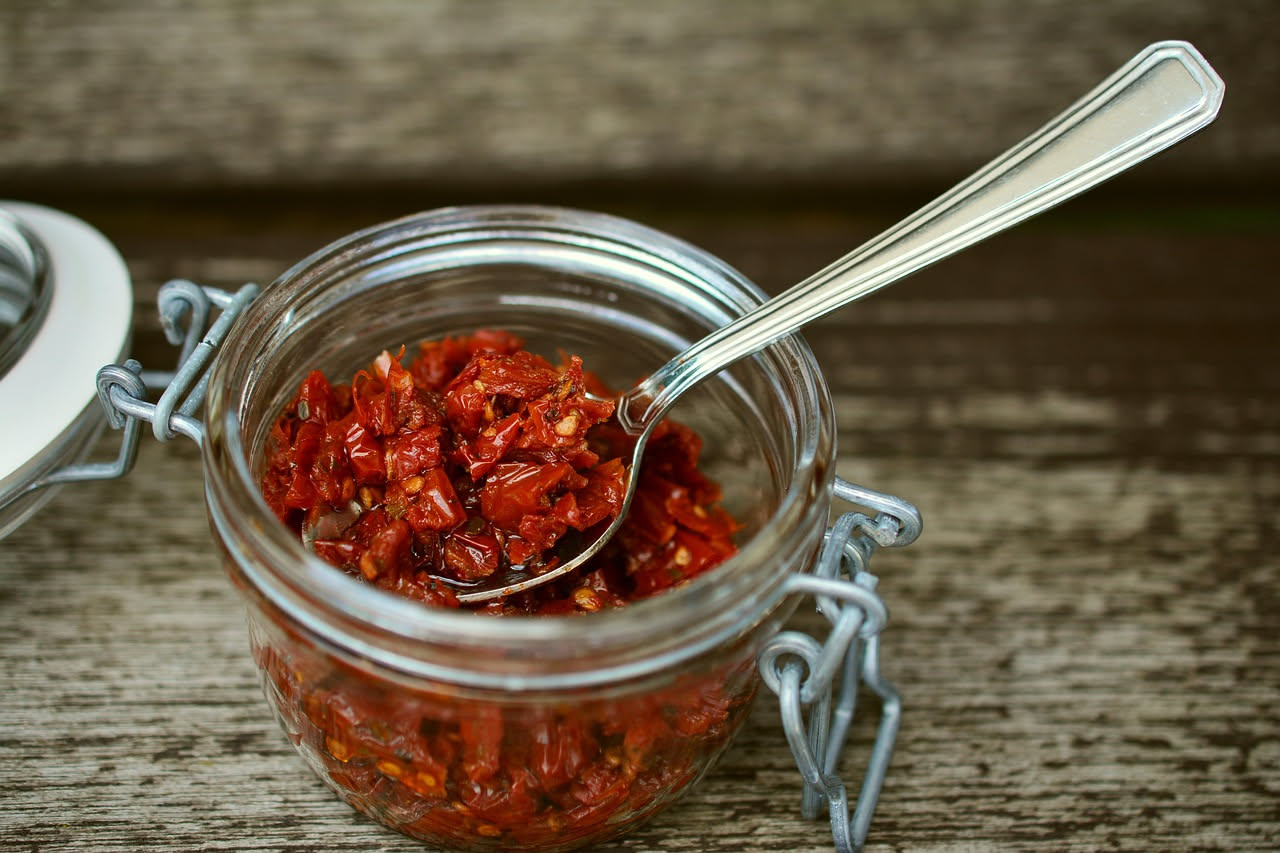 Peperoni rossi e gialli secchi in una padella di ferro, leggermente anneriti sui bordi, con gocce di olio lucido e aglio affettato visibile tra i pezzi