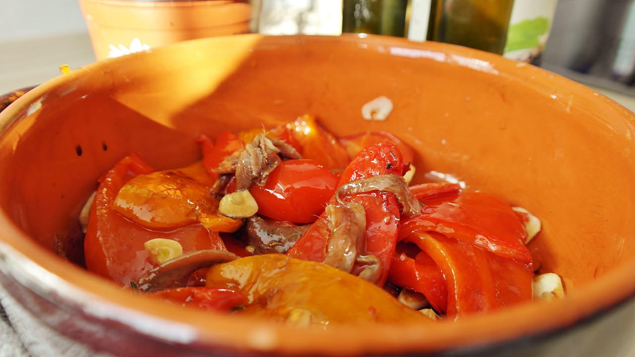 Peperoni cruschi rossi e scuri ripieni di acciughe salate su un piatto bianco, con gocce di olio d'oliva, fotografati da vicino