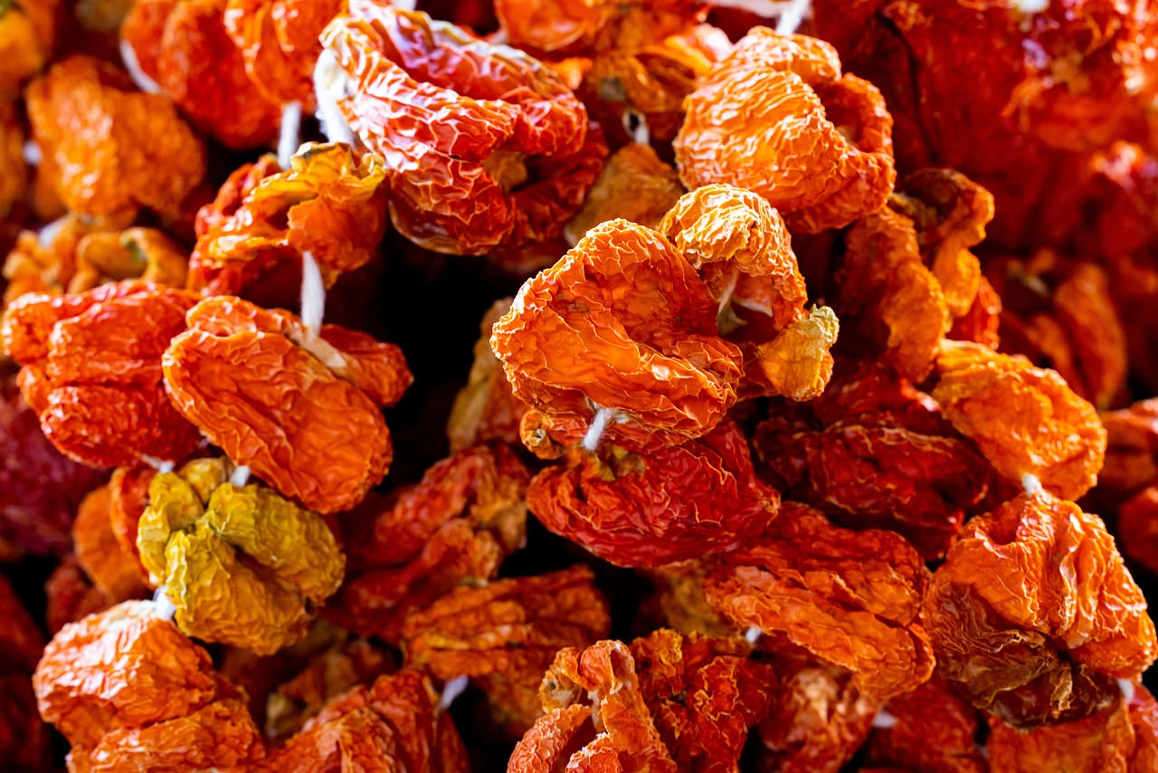 Peperoni cruschi friulani di colore rosso scuro, raggrinziti e lucidi, disposti su un piatto di ceramica bianca accanto a un bicchiere d'acqua e una ciotola di sale grosso