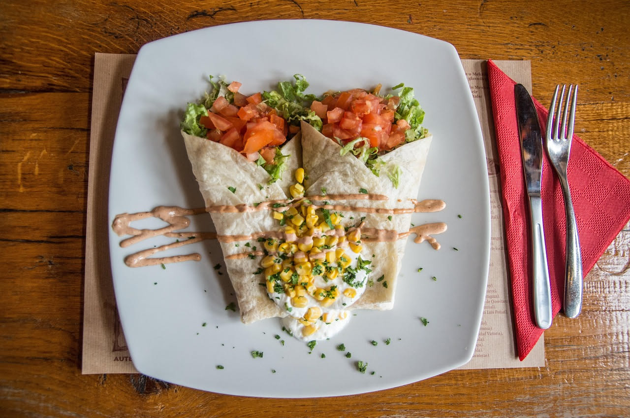 Piadina ripiena rotonda e dorata su piatto bianco, tagliata a metà mostrando il ripieno di prosciutto, formaggio e verdure verdi, con vapore ancora visibile