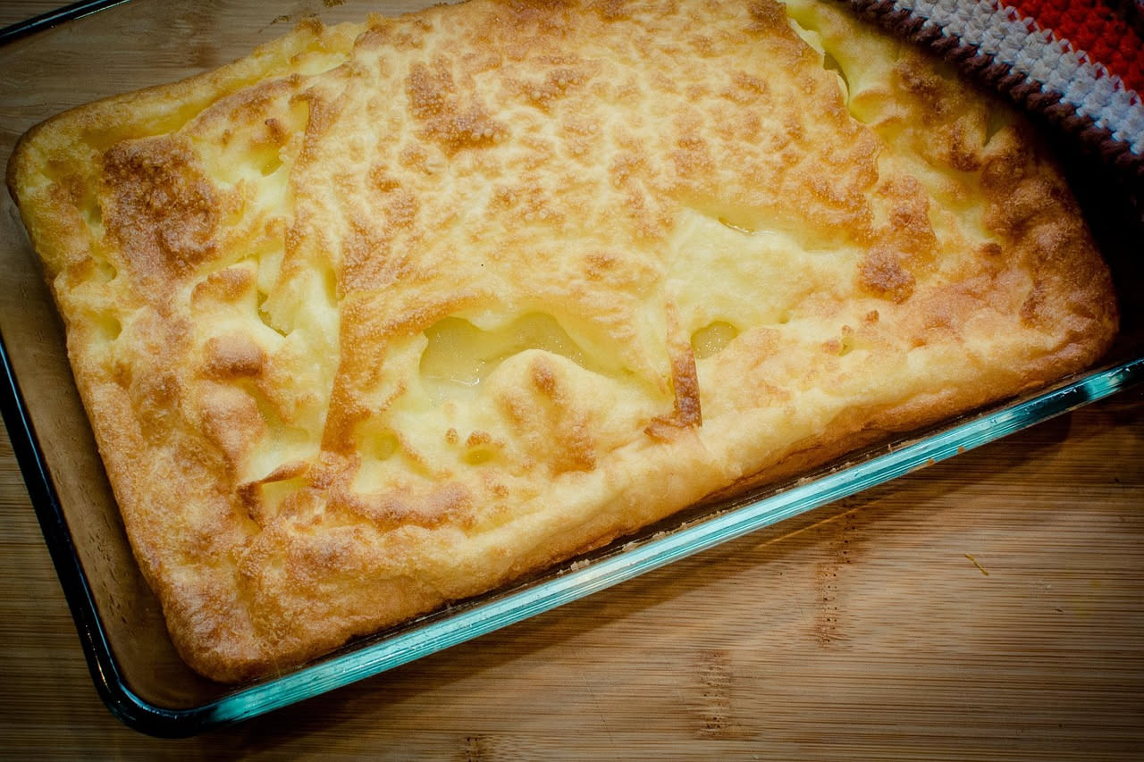 Polenta alla romana cremosa di colore giallo dorato, servita in un piatto fondo bianco, con un filo di burro che fonde in superficie e una spolverata di pepe nero