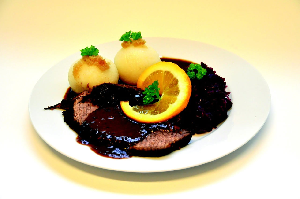 Piatto bianco con polenta cremosa giallo-oro al centro, brasato di manzo scuro e succoso adagiato sopra, salsa di cottura bruno-rossastra intorno, guarnito con prezzemolo fresco verde