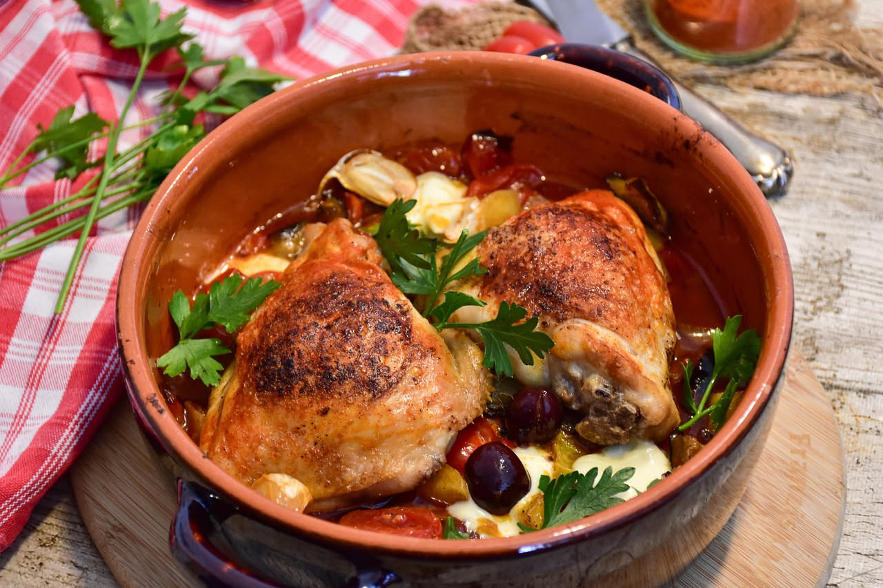 Pollo al cacciatore in pentola di coccio: pezzi di petto e coscia dorati in sugo rosso con pomodori, peperoni rossi e gialli, cipolla bianca e foglie di rosmarino fresco
