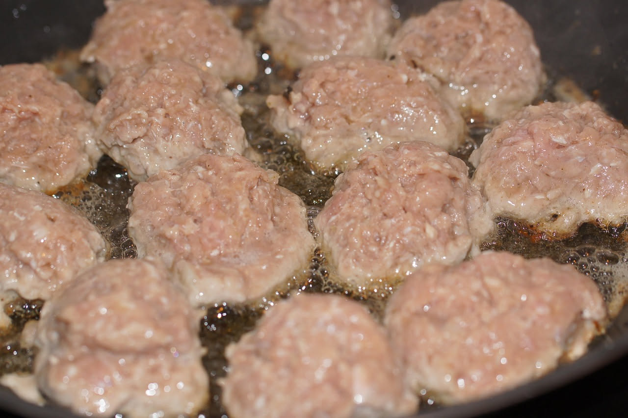 Polpette di carne e pane dorate in un piatto bianco, con una salsa di pomodoro intorno, guarnite con prezzemolo fresco tritato, su una tavola di legno naturale