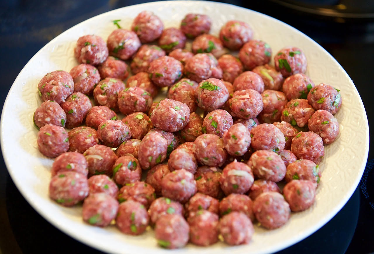 Polpette dorate e soffici in un piatto bianco con sugo di pomodoro, contorno di insalata verde e una goccia di parmigiano grattugiato in superficie