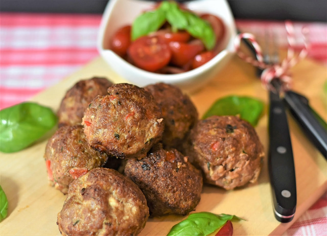 Polpettine di carne dorate e croccanti in una padella di ferro, circondate da salsa di pomodoro, con un cucchiaio di legno e basilico fresco accanto