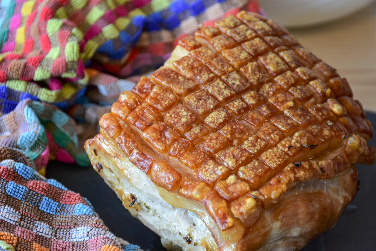 Porchetta dell'Emilia cruda in una teglia di ghisa, circondata da carote, sedano e rosmarino, prima della cottura al forno