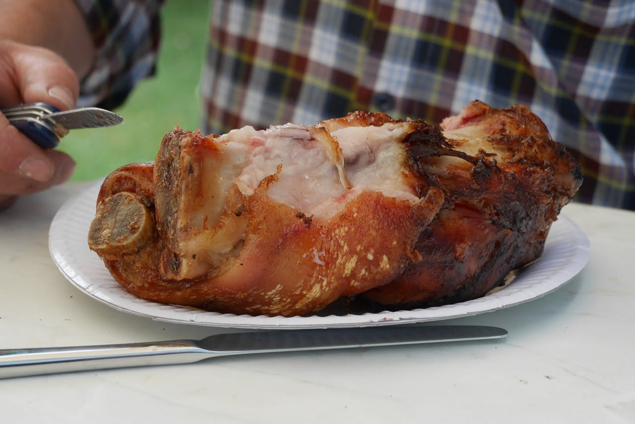 Porchetta intera cotta al forno con pelle croccante dorata, circondata da rosmarino fresco e aglio, affettata su un tagliere di legno