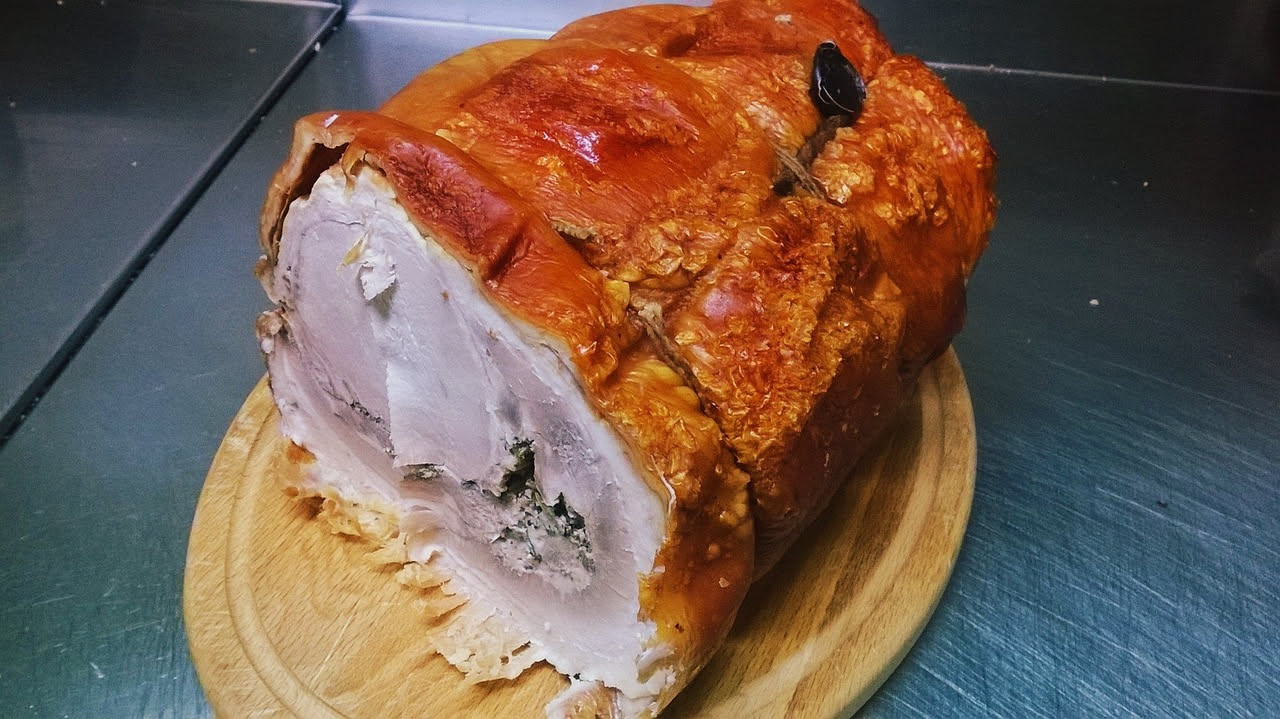 Porchetta intera ricoperta di crosta salata dorata e croccante, con rosmarino fresco, affettata al centro per mostrare la carne succosa all'interno