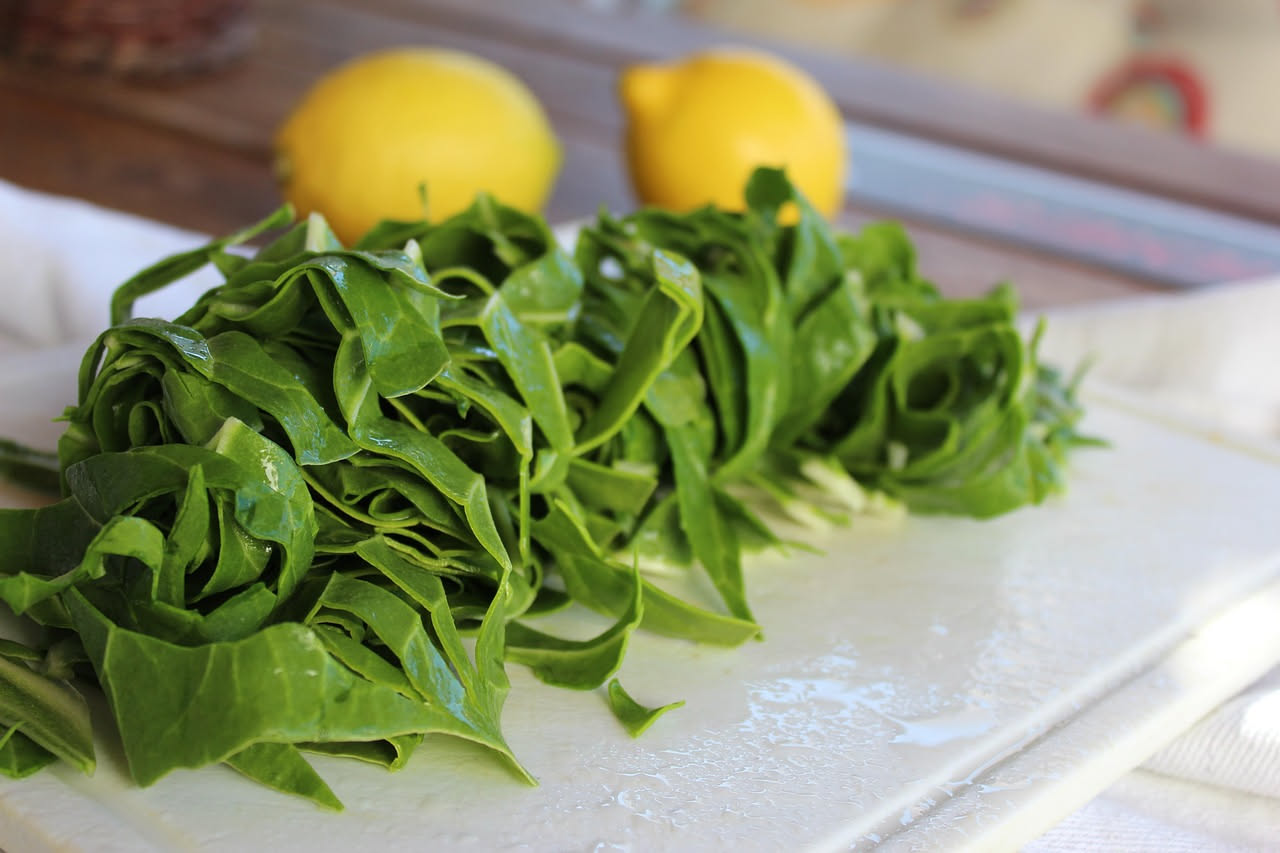 Puntarelle crude verdi e bianche arrangiate su un piatto bianco con filetti di acciuga e salsa dorata in una ciotola di ceramica accanto